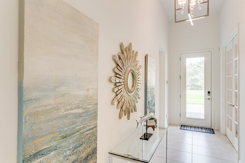Inside of the Kellen model foyer. Tile flooring and white walls. Foyer has a small glass table in it. In the background you can see the front door.