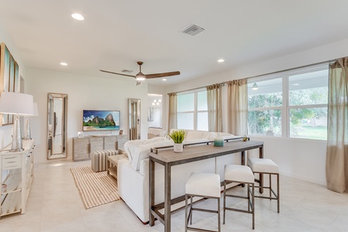Inside of the Kellen model living room. Tile flooring and white walls. This photo of the living room shows a tall table with barstools behind the couch.