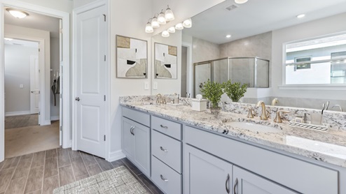 Inside of the Shelby model bathroom two. This angle of the bathroom shows a double vanity with grey cabinets and off-white countertops with silver hardware.