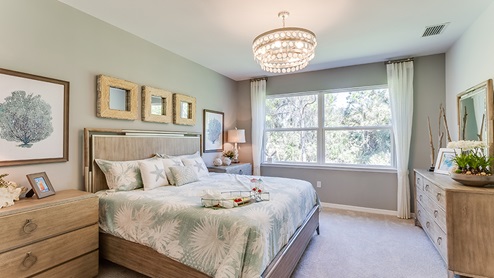 Inside of the Jaden model bedroom one. Crème carpets with teal walls. Room contains a bed with nightstands on either side, dresser, and window.