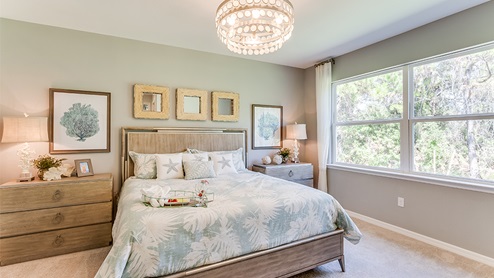 Inside of the Jaden model bedroom one. Crème carpets with teal walls. Room contains a bed with nightstands on either side, dresser, and window.