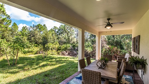 Outside of the Jaden model. Back patio with a six-person dining table, two armchairs, and fan.