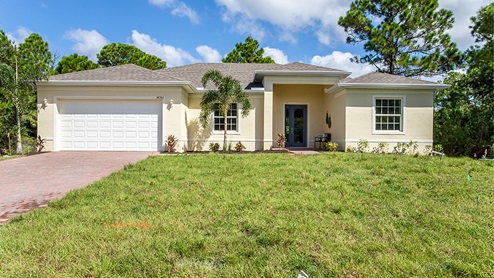 Outside of the Jaden model. Yellow house with two car garage, two windows, and front door. Mixed paver driveway.