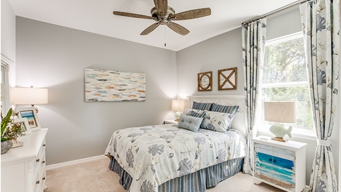 Inside of the Jaden model bedroom two. Crème carpets and grey walls. Room contains a bed with nightstands on either side, dresser, and window.
