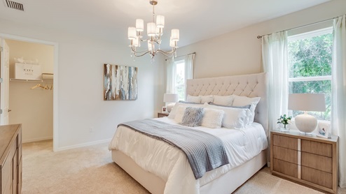 Inside of the Kellen model bedroom one. Crème carpet and white walls. Room contains a bed with nightstands on either side, dresser, and window. Room also has a walk-in closet.