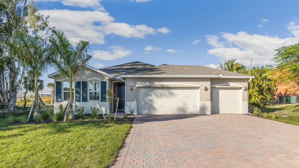 Outside of the Delray model B. Blue home with three garage, one window with shutters, and front door. Mixed paver driveway.