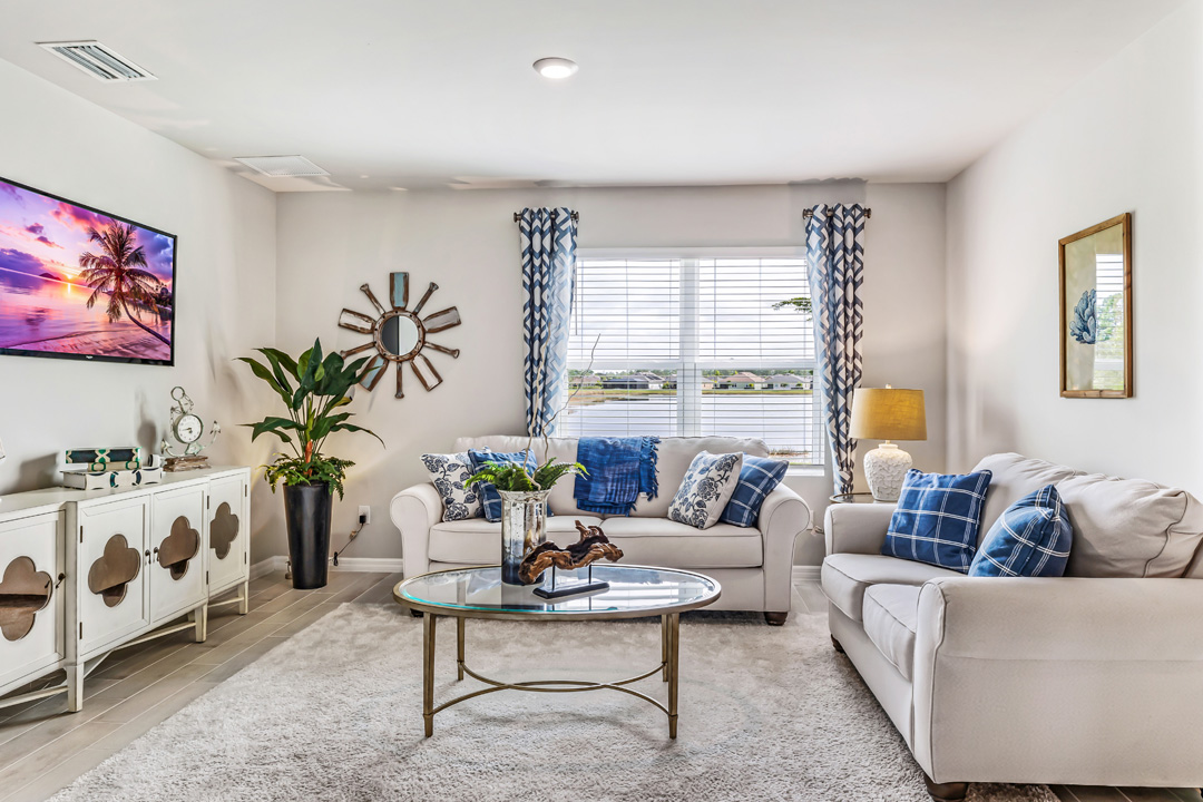 Inside of the Cali model living room. Another angle of the living room, this angle shows another window as well as a TV, storage shelf, and a small plant in the corner of the room.