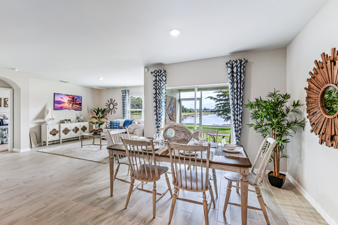 Inside of the Cali model dining room. The dining room contains a six-person dining table and chairs. The living room can be seen in the background as well as the sliding glass door that leads to the back patio.