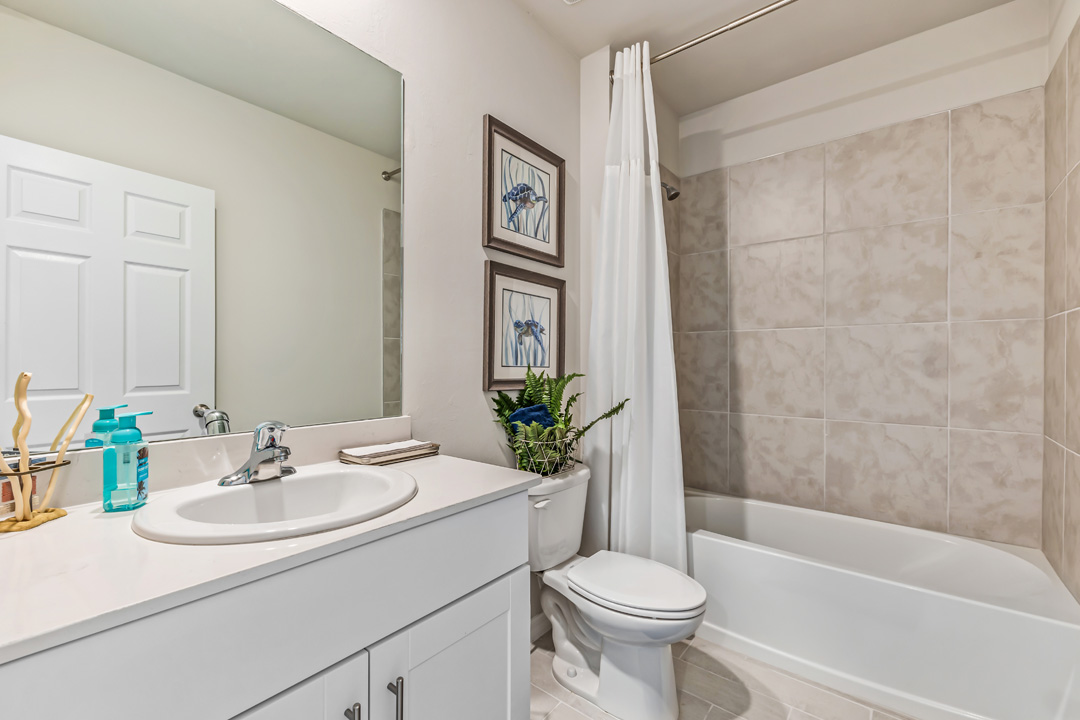 Inside of the Cali model bathroom two. This bathroom also has a shower-tub combo with grey tile and white tub. Bathroom contains a single vanity with white countertops and cabinets with silver hardware. White toilet is between the vanity and tub.