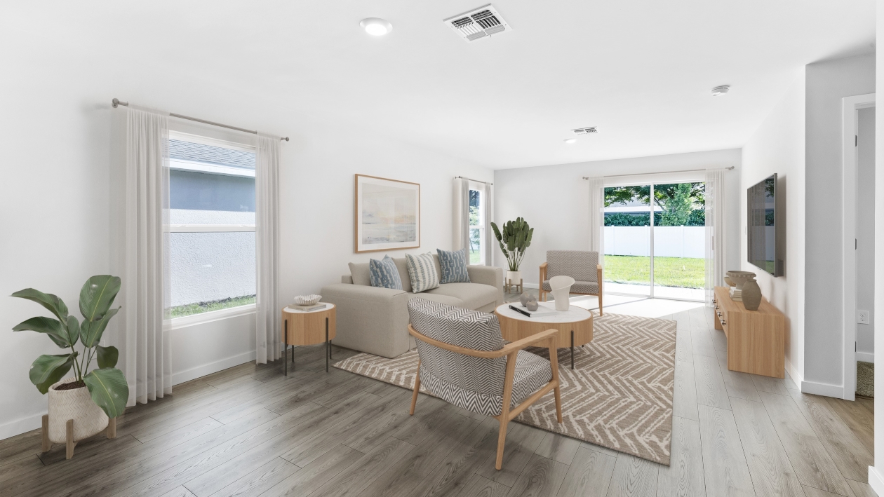Inside of the Dundee model living room. Revwood floors and white walls. Room contains one small couch, two chairs, a coffee table, and a TV. Room also connects to the backyard area.