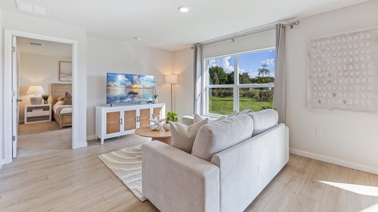 Inside the Freeport living room. Revwood floors and off-white walls. Contains one large couch, one small coffee table, TV, and lamp in the corner.