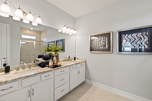 Inside of the Kellen bathroom. Dual vanity with white countertops and cabinets with silver hardware.