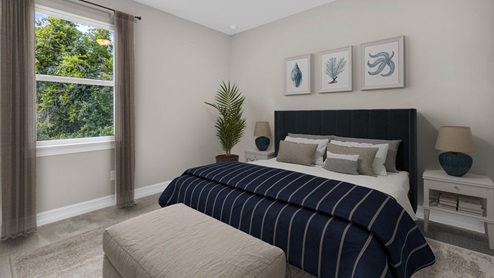 Inside of the Delray B model bedroom two. Grey carpet with off-white walls. Room contains one large bed with nightstands on either side and a bench at the end of the bed. Room also contains a window.