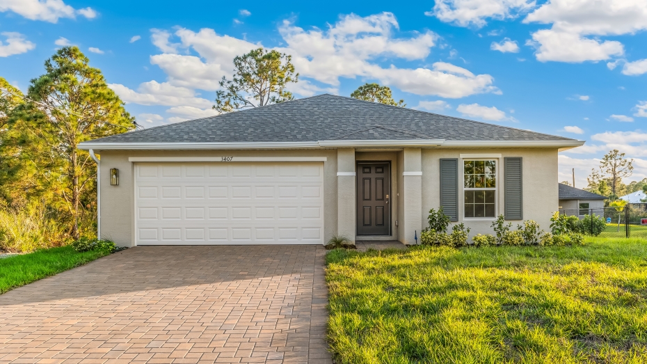 Outside of the Boardwalk B model. Beige home with two car garage, window with shutters, and front door. Mixed paver driveway.