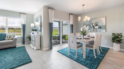 Inside of the Cali model dining area. Wood tile flooring and teal walls. Dining area contains a six-person dining table with a hanging light fixture above it. In the background a sliding glass door that leads to the back patio can be seen as well as an open area that contains the living room furniture.