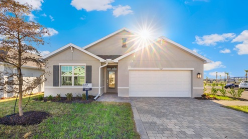 Outside of the Cali D model. Grey home with a two car garage, one window with shutters, and front door. Mixed pavers driveway.