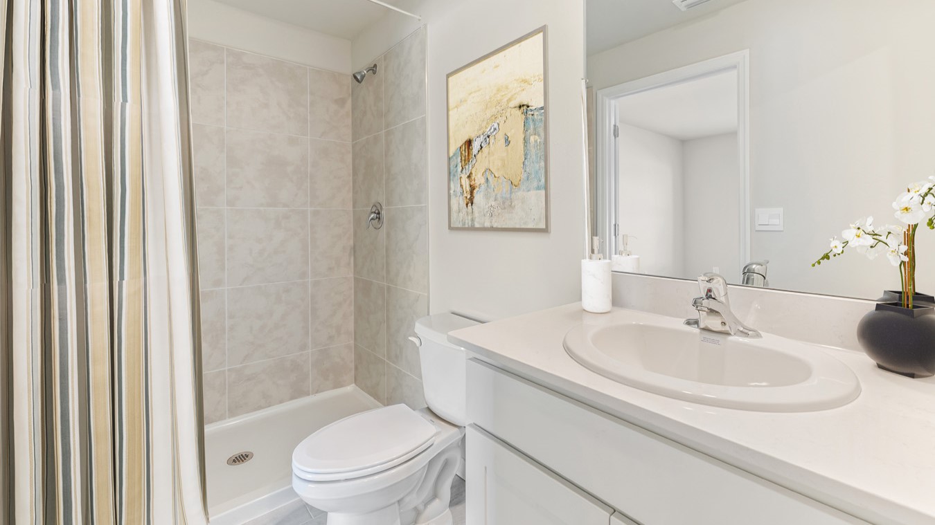 Inside of the Freeport model bathroom. Off-white walls, white countertops with silver hardware. White toilet as well as white bathtub shower combo.