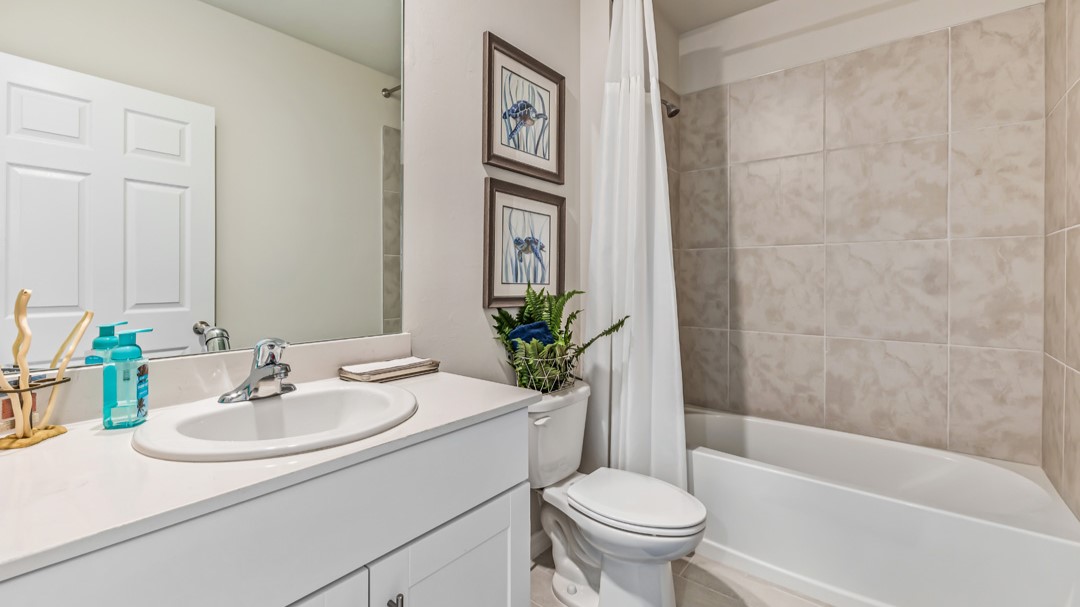 Inside of the Cali model bathroom two. This bathroom also has a shower-tub combo with grey tile and white tub. Bathroom contains a single vanity with white countertops and cabinets with silver hardware. White toilet is between the vanity and tub.