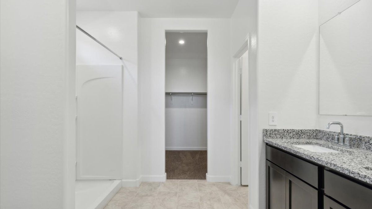 Modern primary bathroom with double vanity, granite countertops with a walk-in shower and a walk-in closet.