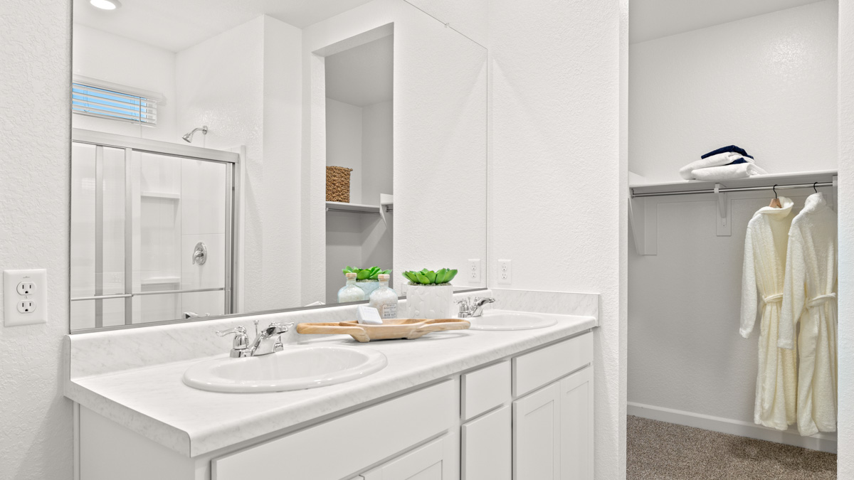 Modern primary bathroom with double vanities, porcelain countertops with a walk-in shower and a walk-in closet.