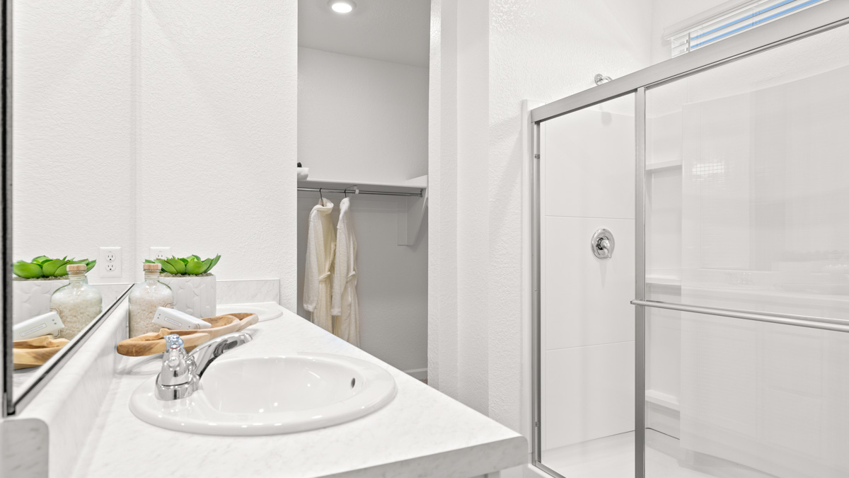 Modern primary bathroom with double vanities, porcelain countertops with a walk-in shower and a walk-in closet.