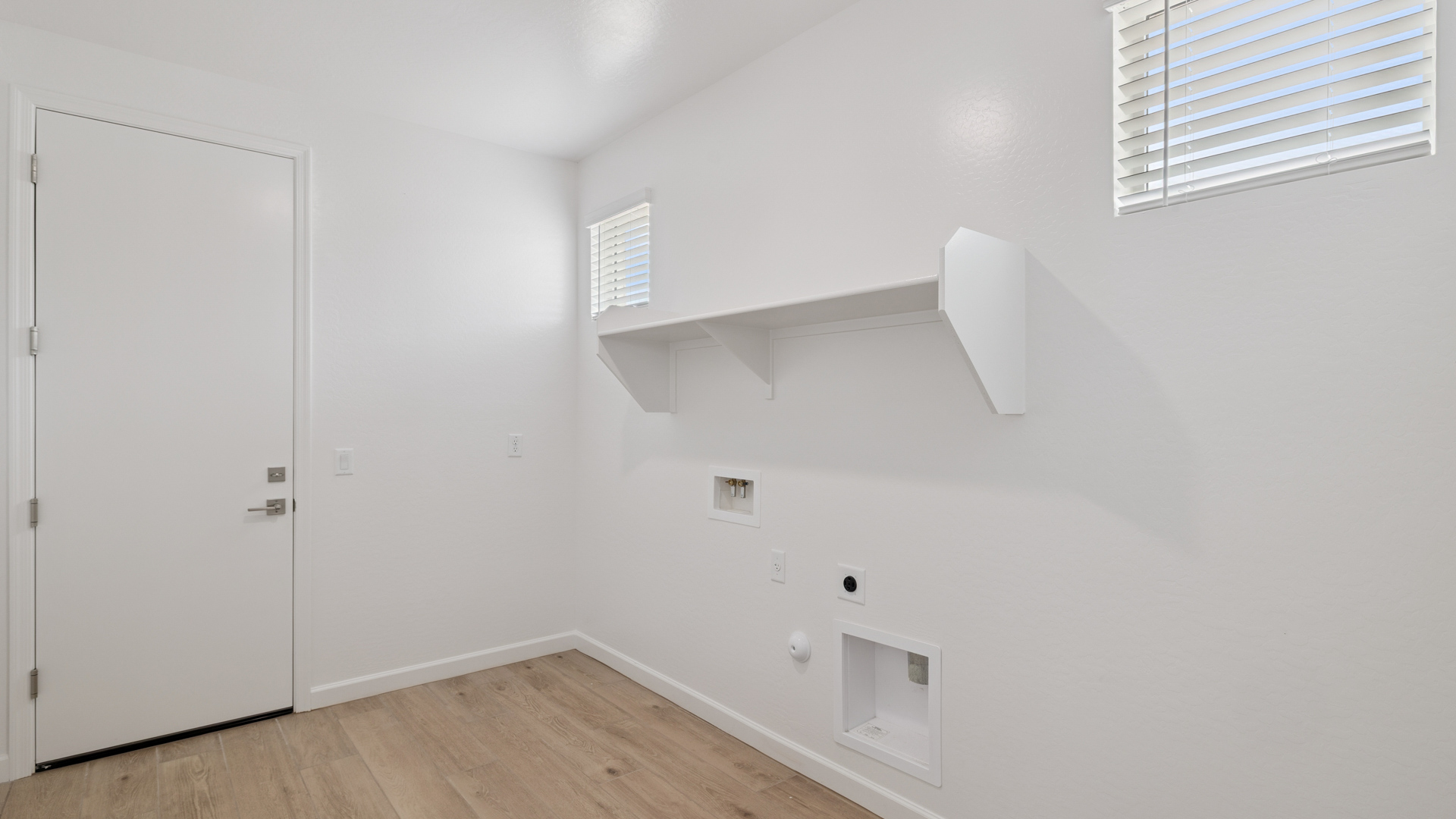 Spacious laundry room with washer and dryer connections and shelving for storage.