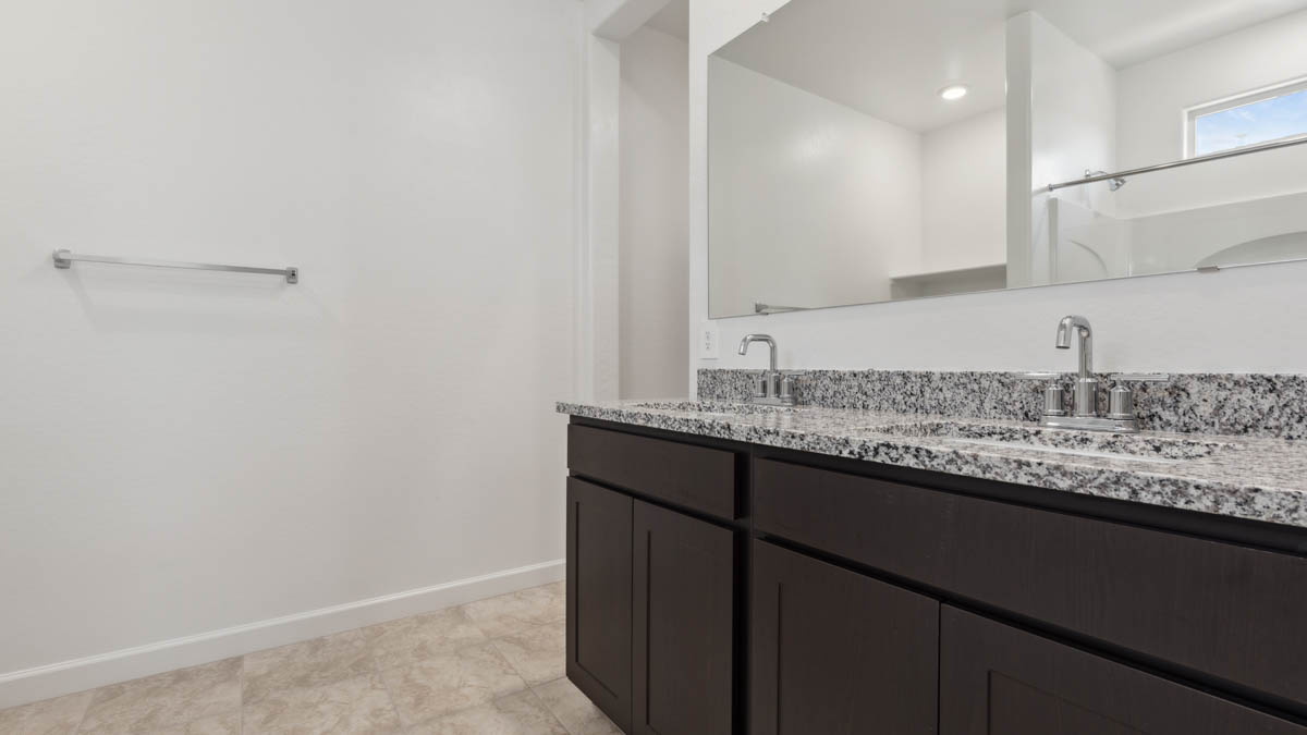 Modern primary bathroom with double vanity, granite countertops with a walk-in shower and a walk-in closet.