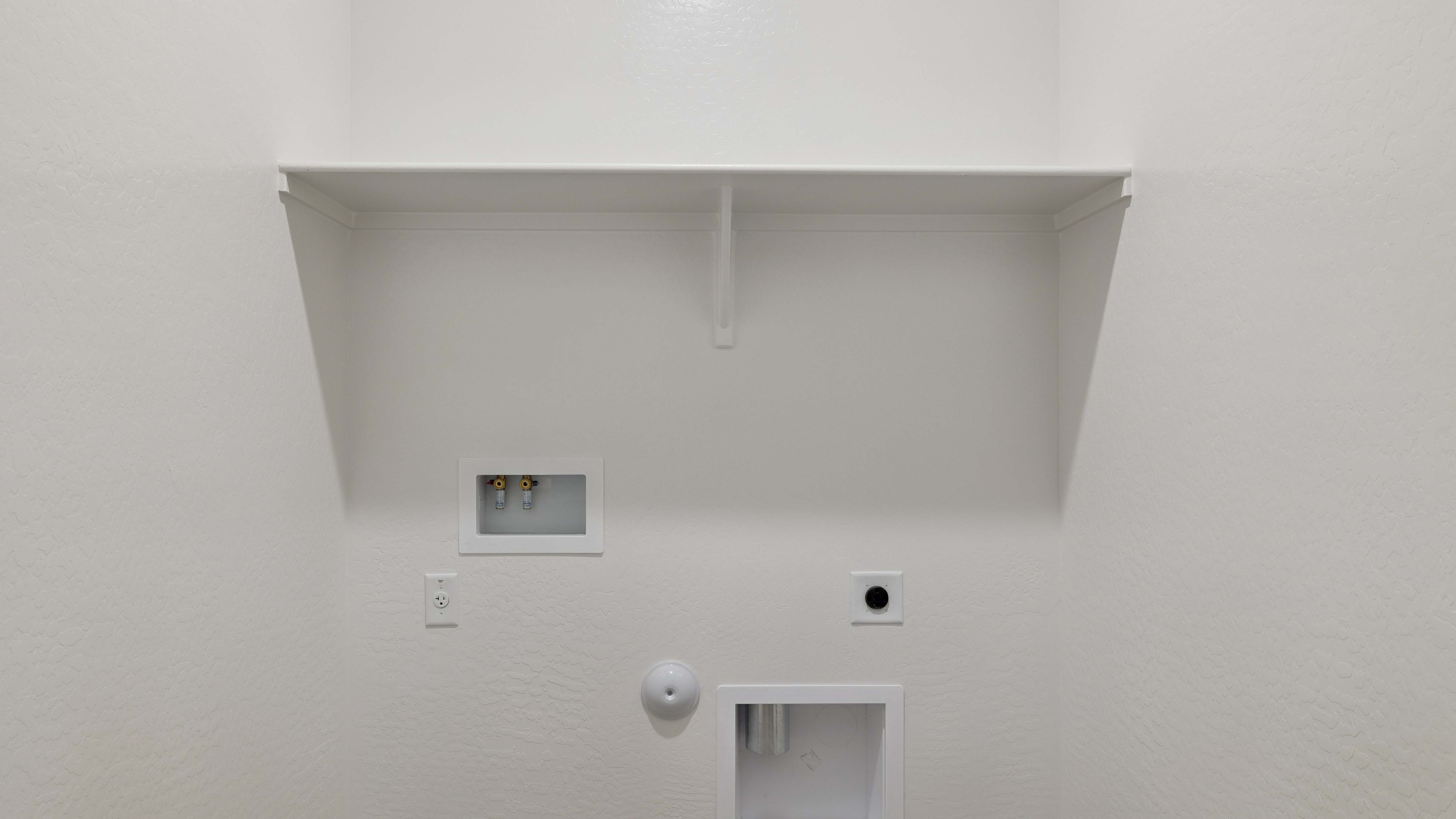 Spacious laundry room with washer and dryer connections and shelving for storage.