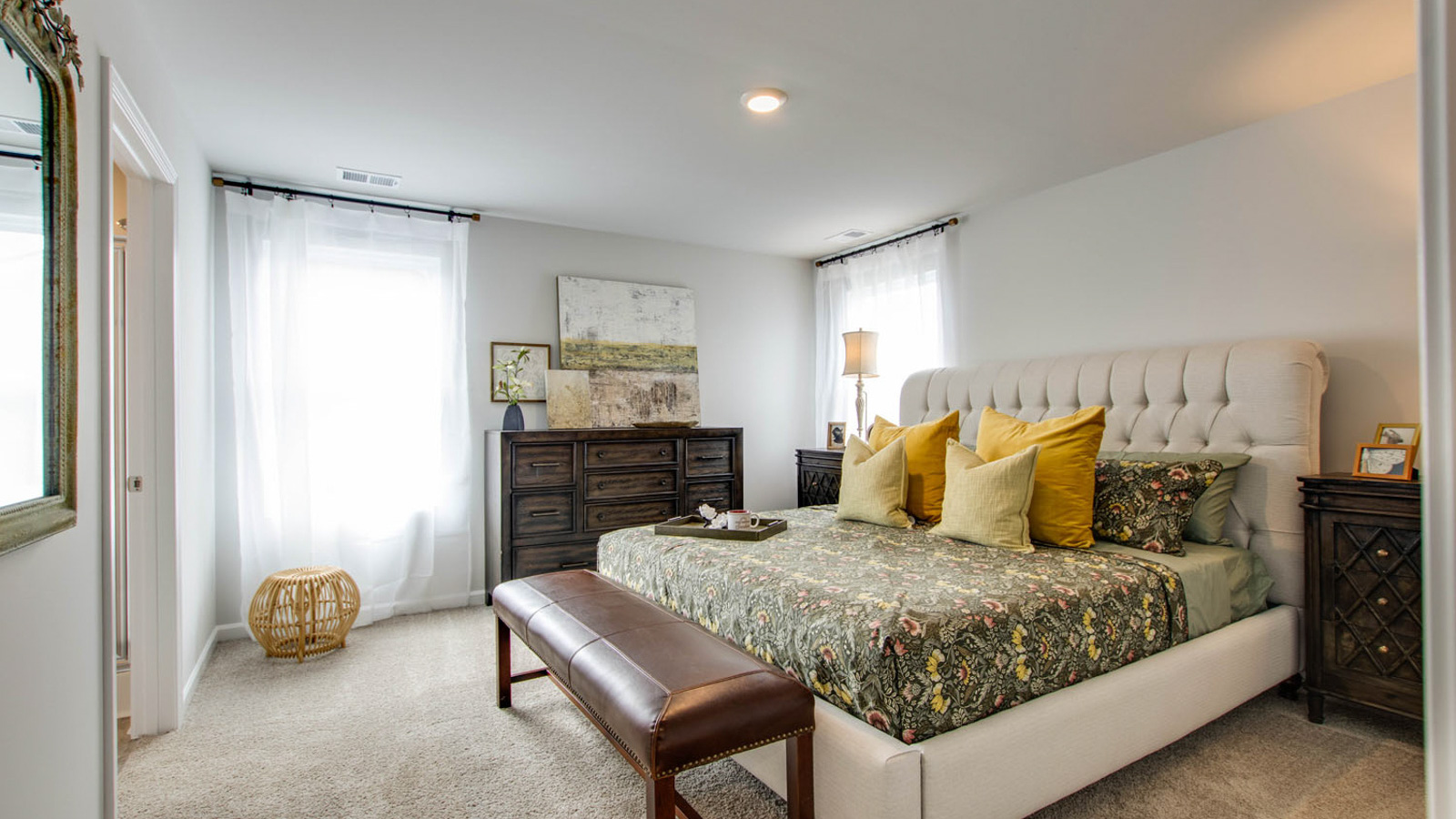 Spacious primary bedroom with beige carpet, white walls and two windows