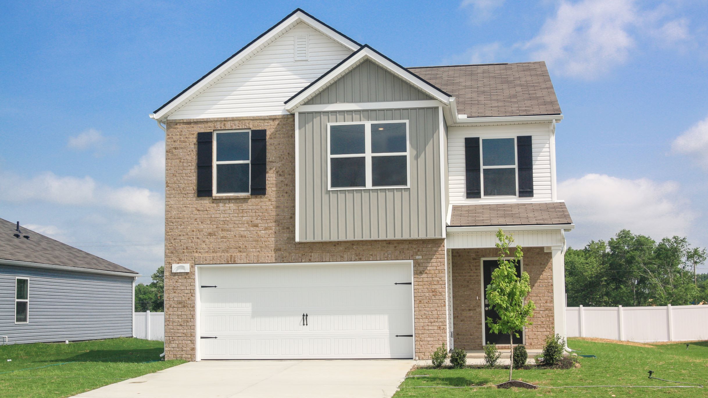 front exterior of a two story home with grey siding, brick and a two car garage