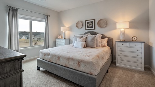 cali plan model in twin lakes community primary bedroom with carpet flooring, space for a king-size bed and additional bedroom furniture, and a large double-window overlooking the backyard