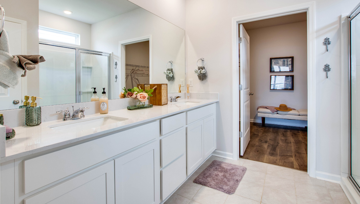 bristol plan primary bathroom with large double-vanity, granite countertops, vinyl flooring, and walk in shower with a glass enclosure in the orchard community