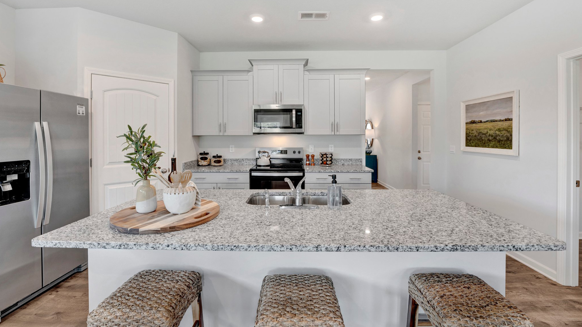 dover plan kitchen with bar seating at the island, granite countertops, tall cabinets with crown and hardware, and stainless steel appliances included in the orchard community