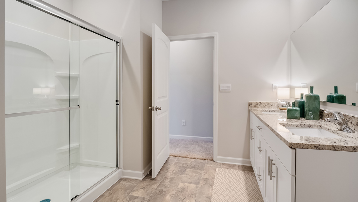lacombe floorplan in indian oaks community primary bathroom with walk-in shower enclosed in glass and a double vanity with large mirror over it