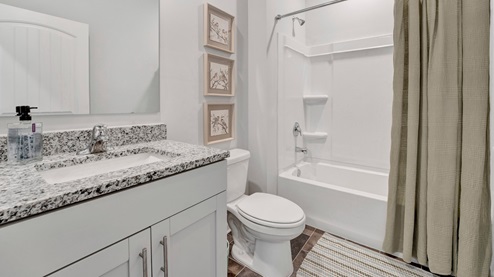 secondary bathroom with tub and shower combination, granite countertops on the vanity, and vinyl flooring