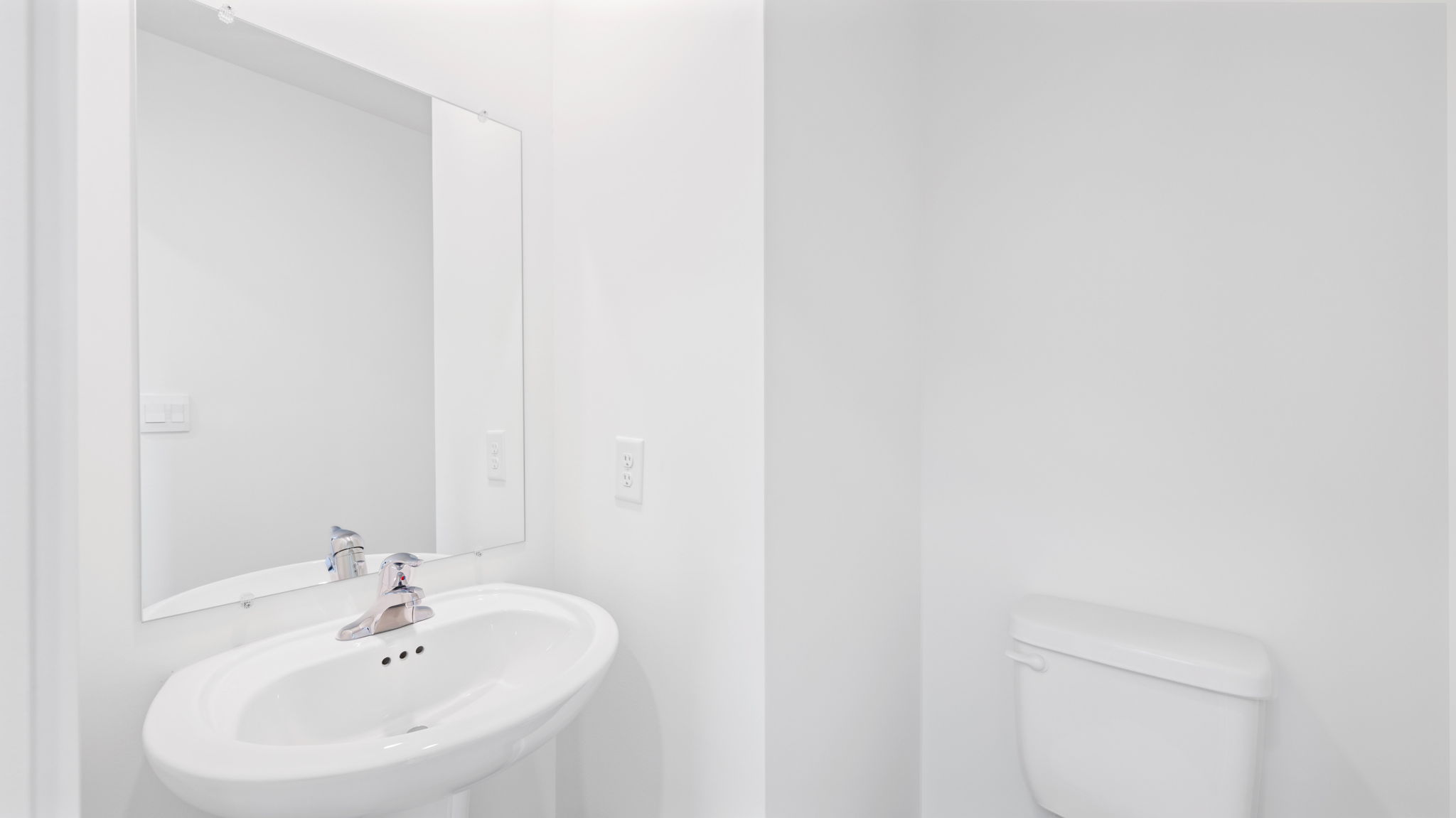 Entry-level half bathroom with pedestal sink, mirror, and clean finishes near the main hallway