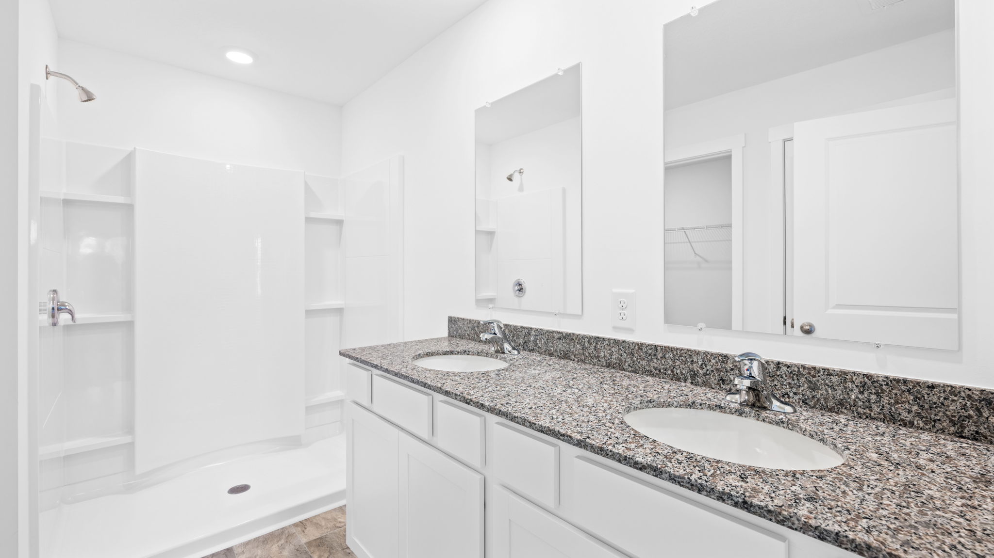 bathroom with dual sink cabinets and shower
