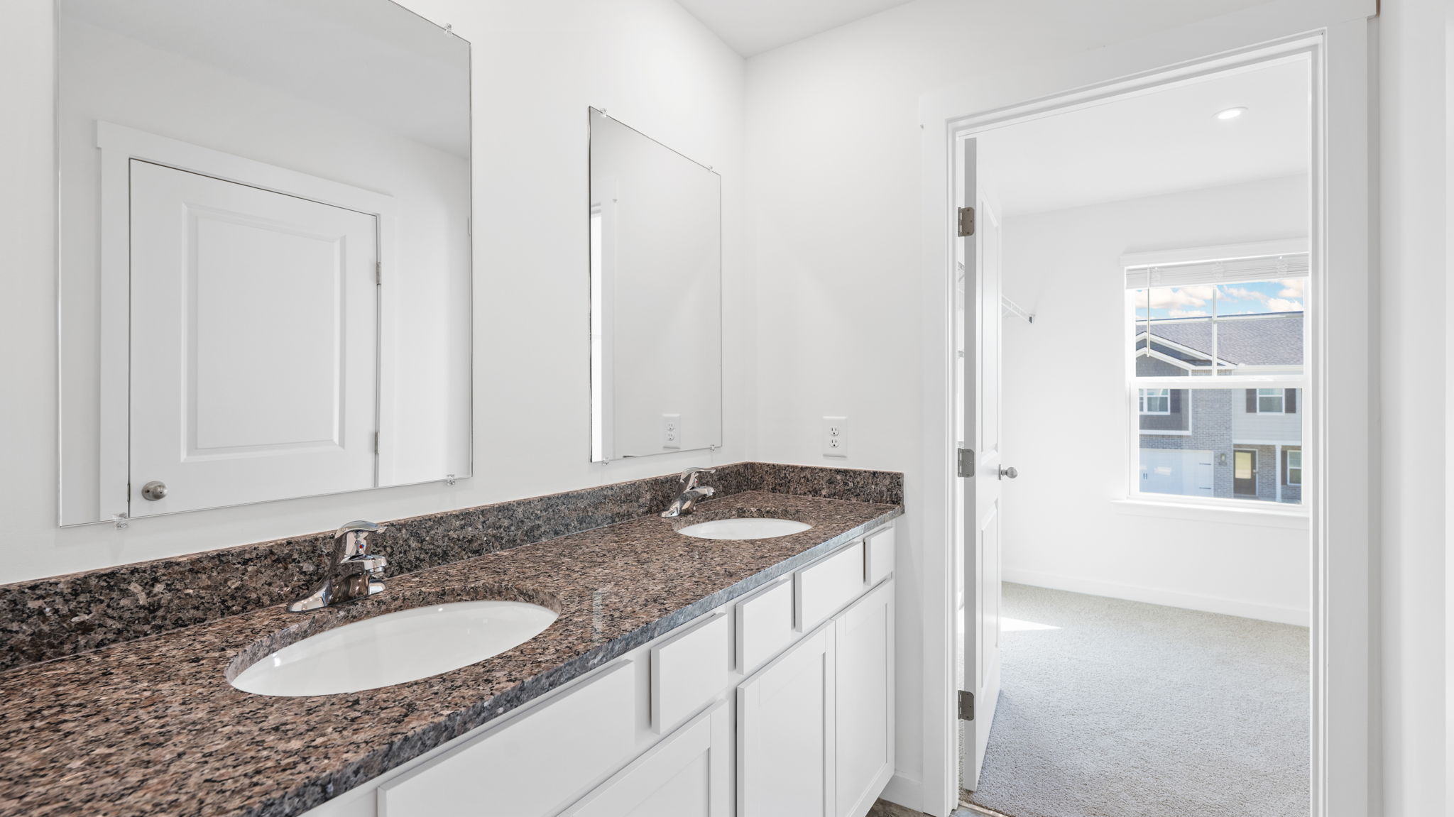 primary bathroom with dual sinks and mirror opening into bedroom