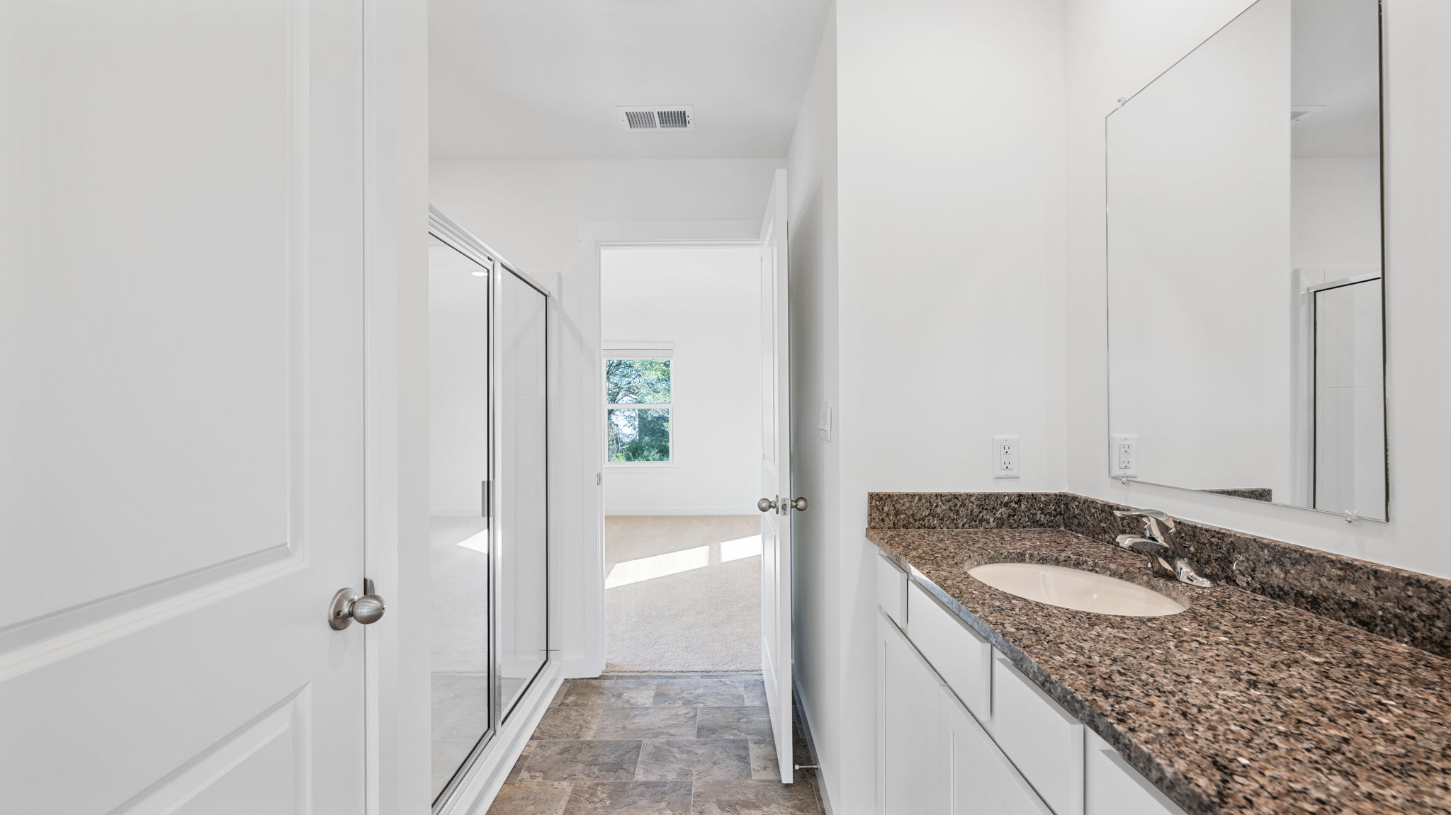 primary bathroom with dual sinks and mirror opening into bedroom