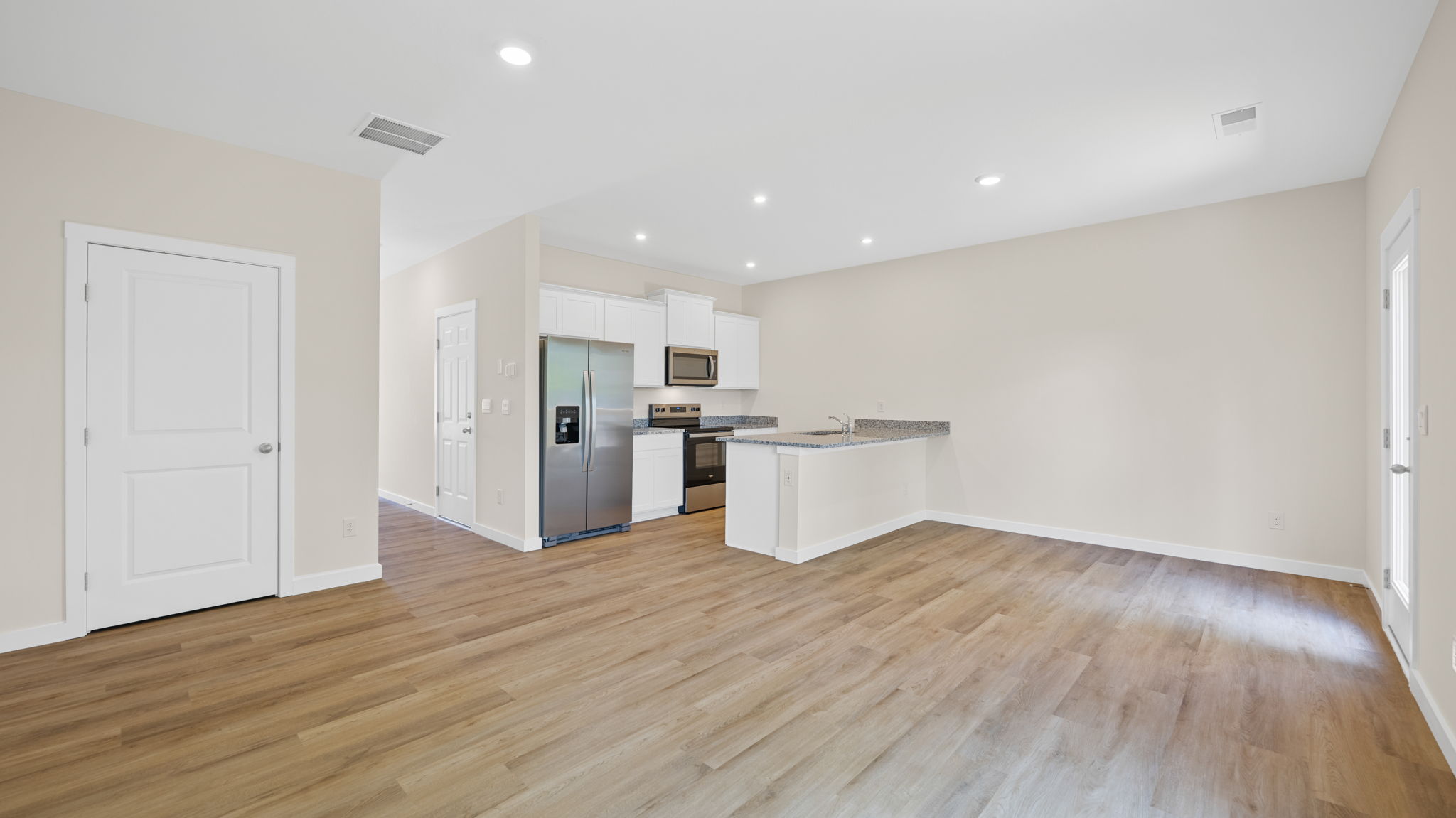 Main living area with clean flooring and natural light connecting to kitchen.