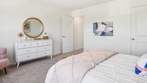 Bedroom with bed and pink bedspread and white dresser