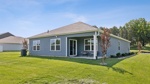 Rear exterior of one level home with blue vinyl siding and a covered patio with sliding glass door entrance to home