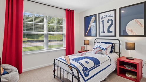 Bedroom staged for young baseball fan with a themed quilt on a twin sized bed and red curtains and a red nightstand