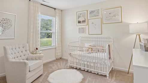 Bedroom staged as a nursey with a white chair, rug, crib, dresser, and ballerina artwork on the walls