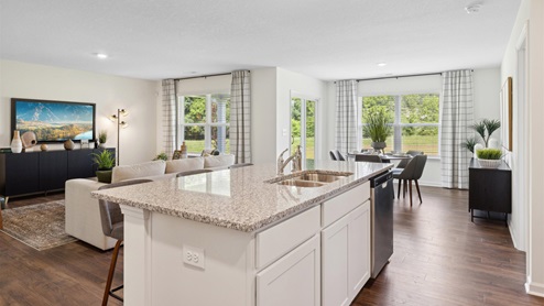 Kitchen island with sink and dishwasher and white cabinets overlooking living space