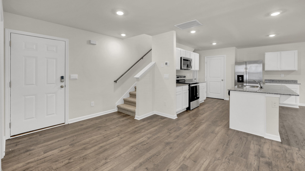 Spacious living room looking toward stairs, modern kitchen island, dining, new appliance suite at Price's Point