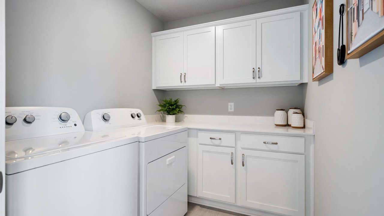 Upper level laundry room with white cabinets and quartz countertops.