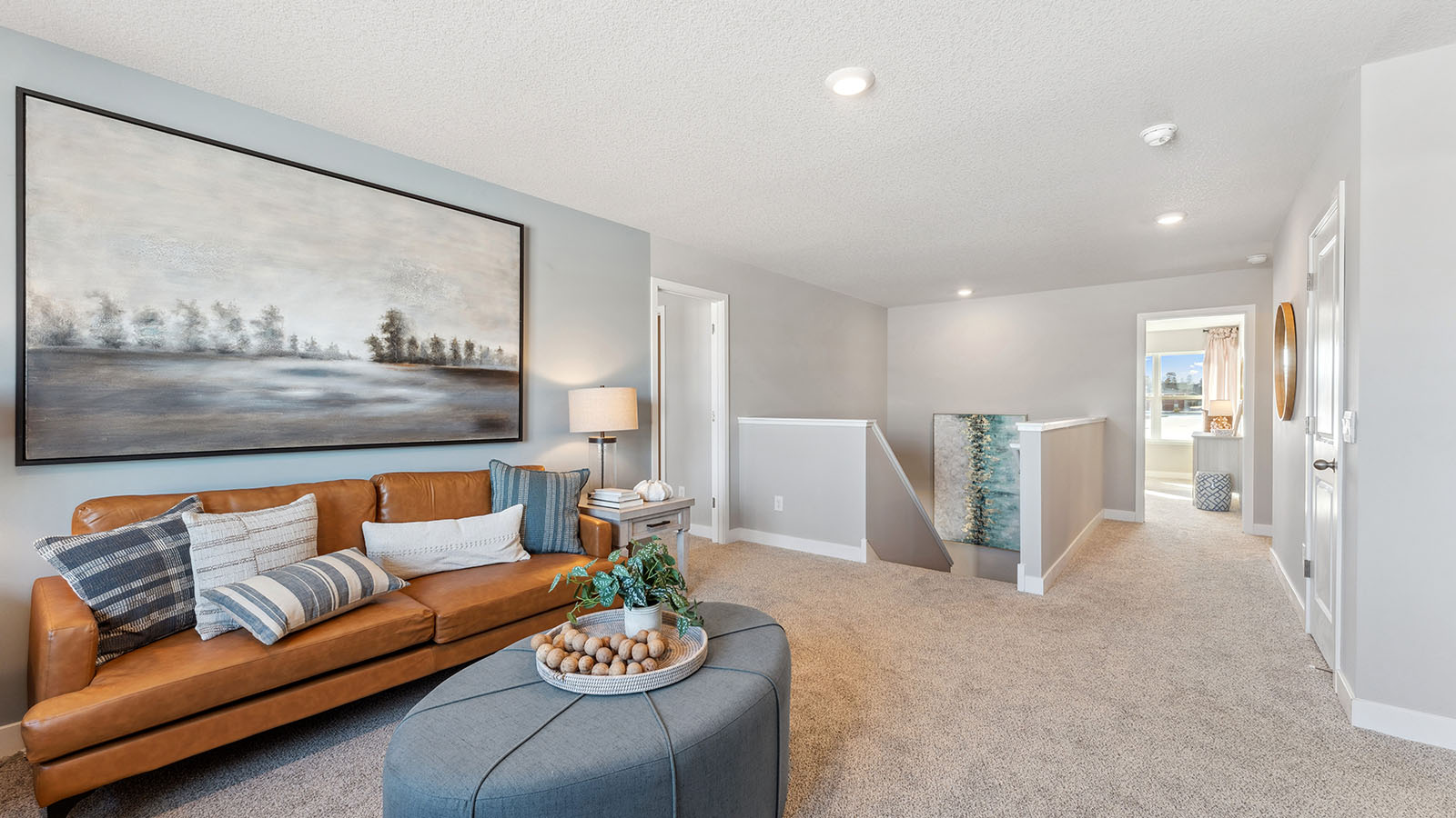 Carpeted upper level loft staged with two brown couches and end tables