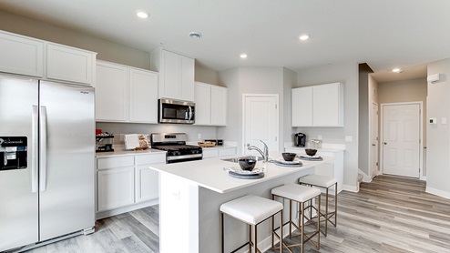 Angled view of kitchen with white cabinetry and stainless steel appliances.