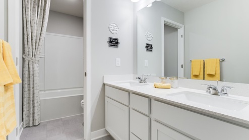 Secondary bathroom with white cabinetry and quartz double vanity.